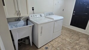 A laundry room with two white washing machines, a sink, and a small table. - Spacious, Pet Friendly Basement Apartment  (Milton)