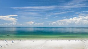Uma praia com águas azul-turquesa cristalinas, um areal dourado e alguns barcos ao longe.