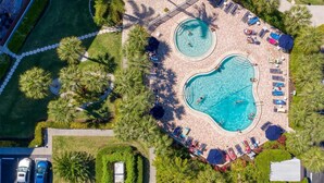 Luchtbeeld van een resort met twee zwembaden, ligbedden en palmbomen.