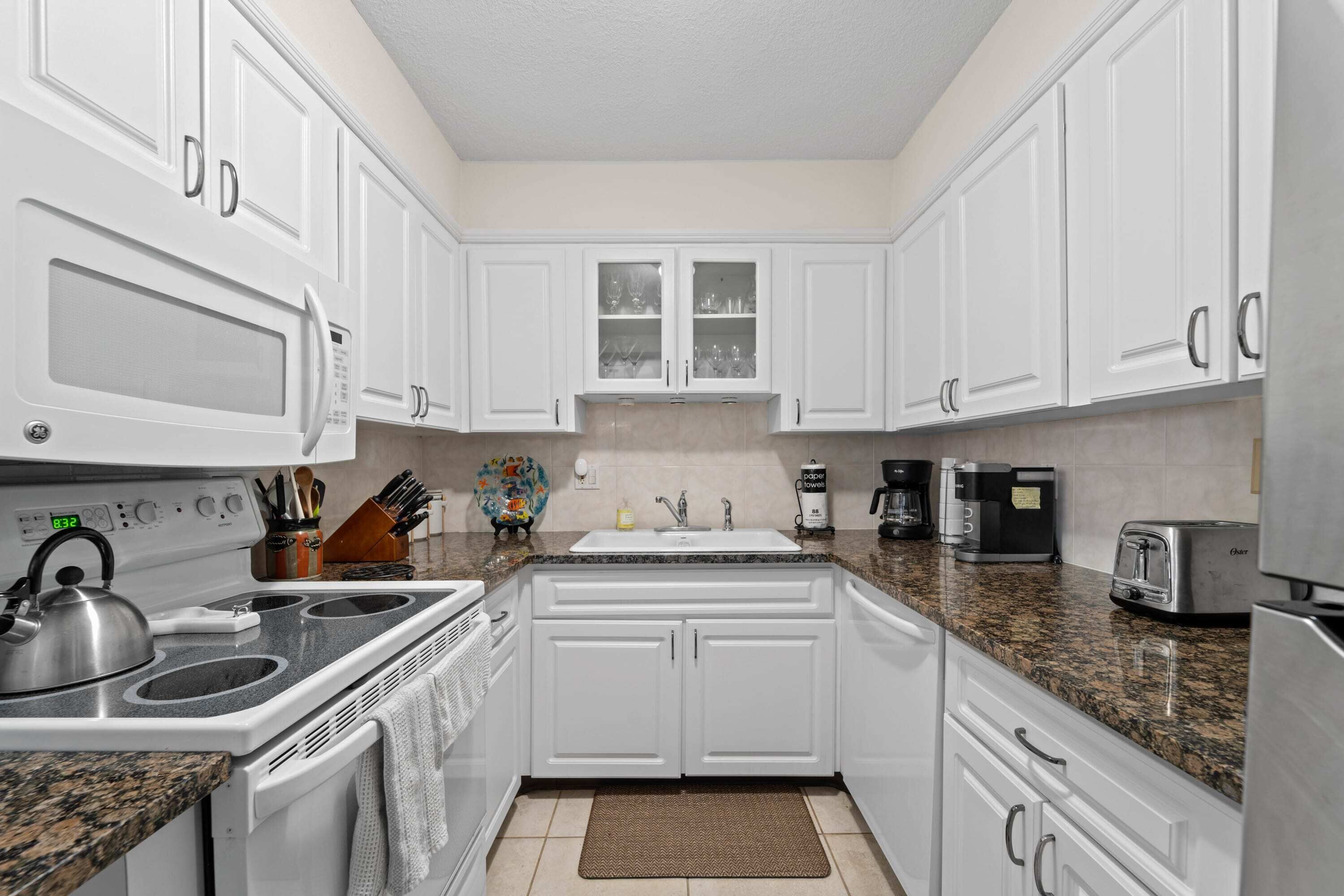 A kitchen with white cabinets, a stove, a microwave, a sink, and a toaster.