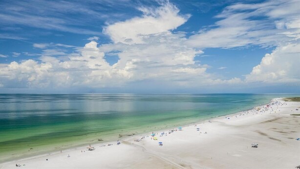 Een strand met helder turquoise water, wit zand en enkele parasols.
