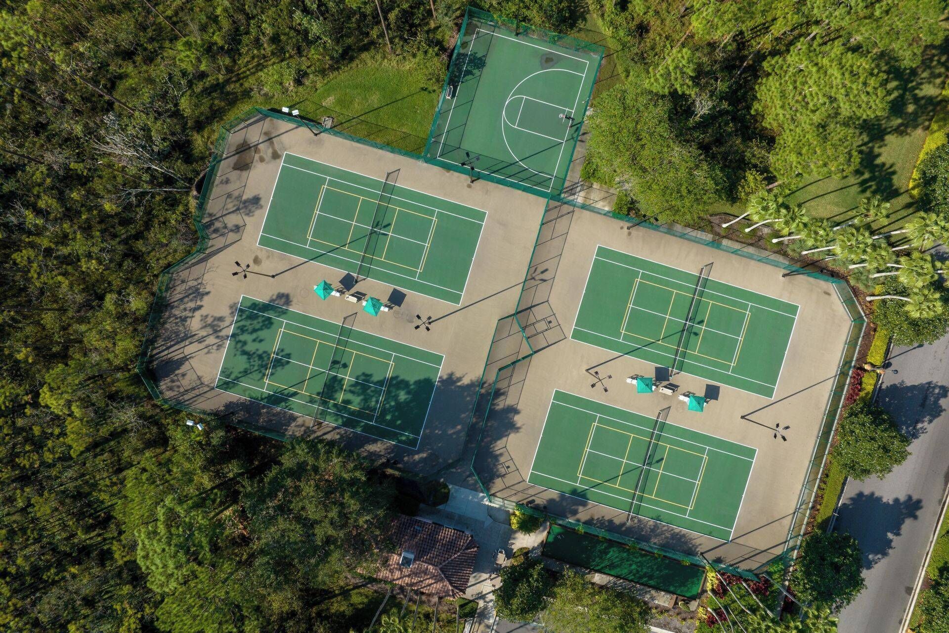 An aerial view of a tennis court complex with multiple courts, surrounded by dense greenery.