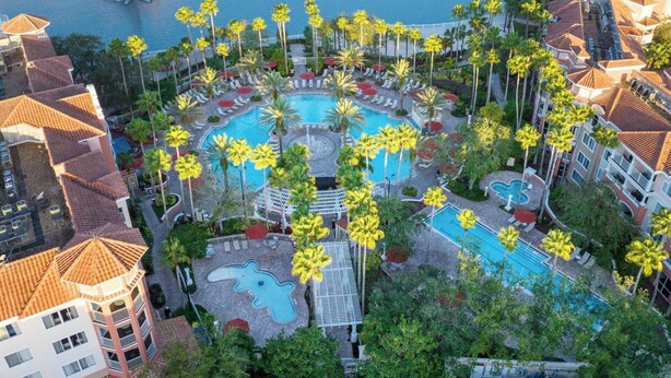 Un resort con varias piscinas, palmeras y un puente sobre el agua.