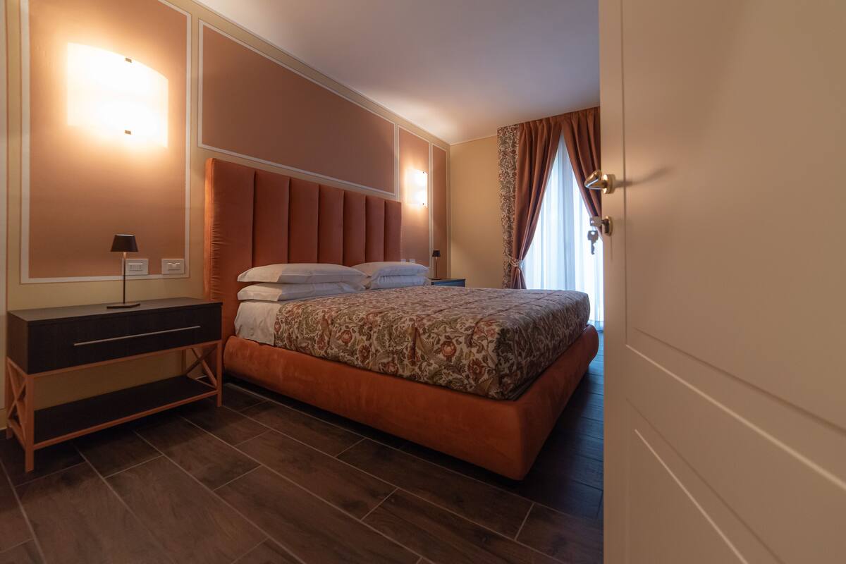 A bedroom with a bed, nightstands, a dresser, and a wall-mounted light fixture.