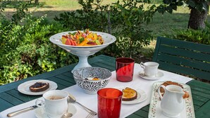 An outdoor dining table set with a variety of food and drink items, surrounded by greenery and a tree. - i castagni (Vigevano)