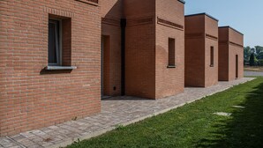 A row of brick buildings with a paved walkway and a grassy area. - i castagni (Vigevano)