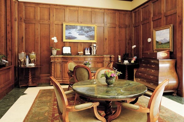A formal dining room with a wooden paneled wall, a round marble table, and classic furniture.