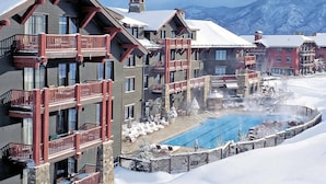 Un hotel con varios balcones, piscina y vistas a montañas nevadas.