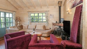 Ein gemütliches Blockhaus-Interieur mit einer Couch, zwei Sesseln, einem Couchtisch, einem Kamin und einem Fenster mit Vorhängen.