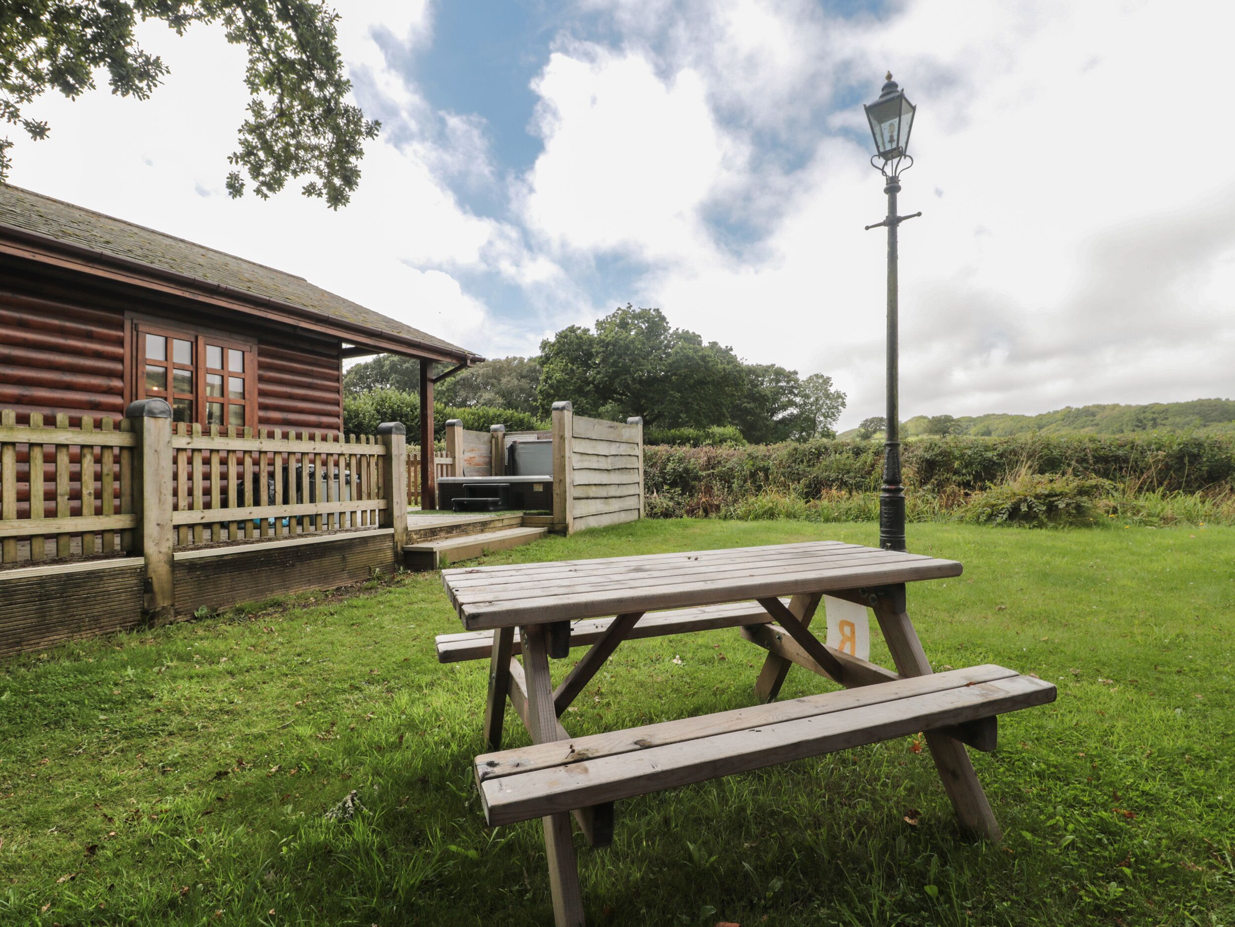 A picnic table in a grassy area with a wooden fence and a building in the background.