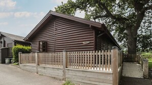 A log cabin with a wooden fence, a paved driveway, and a large tree nearby. - Oaks (Swanage)