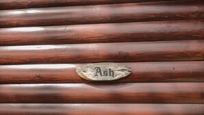 Un mur en bois composé de planches horizontales et une plaque métallique rustique portant le mot « Ash ».