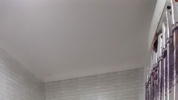 A bedroom with a bed, white curtains, and a brick-patterned wall.