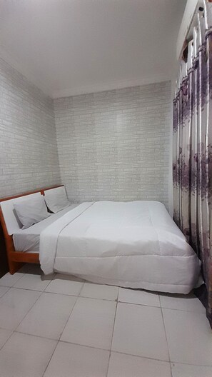 A bedroom with a bed, white curtains, and a brick-patterned wall. - Hotel O Kos Rumah Mirah Syariah (Medan)