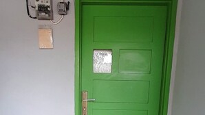 A green door with a welcome mat, a metal rack, and a wall-mounted electrical box.