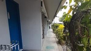 A covered walkway with a blue door, a metal railing, and a potted plant.