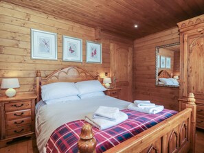 A wooden cabin-style bedroom with a bed, nightstands, a mirror, and framed pictures on the wall. - Walnut (Swanage)