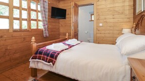 Una habitación de cabaña de madera con una cama, televisión y baño visible a través de una puerta abierta.