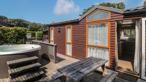 A wooden cabin with a hot tub, picnic table, and a covered outdoor kitchen.