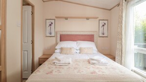 A bedroom with a bed, two nightstands, a window with curtains, and two wall-mounted pictures.