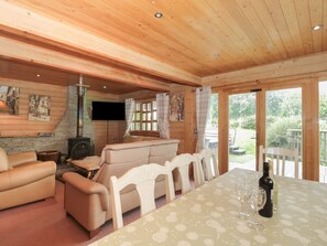 A cozy cabin interior with a sofa, chairs, a dining table, a fireplace, and a TV mounted on the wall. - Pine (Swanage)