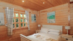 Ein Schlafzimmer einer Holzhütte mit einem Bett, Nachttischen und einem Fenster mit Vorhängen.