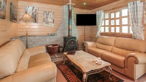 Ein gemütliches Wohnzimmer mit zwei Ledersofas, einem Couchtisch, einem Kamin, einem Flachbildfernseher und einem fenster mit Vorhängen.