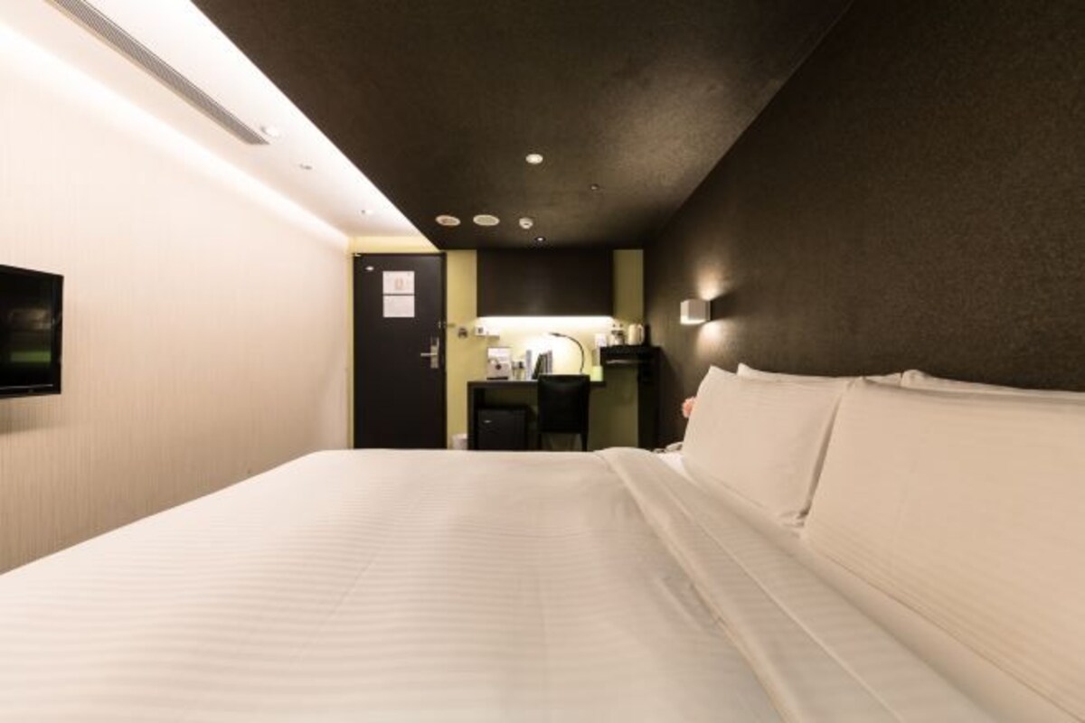 A hotel room with a bed, a desk, and a television on the wall.