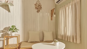 Een kamer met een ronde witte tafel, een houten bankje, een aan de muur hangende dreamcatcher en een bloempot met plant.
