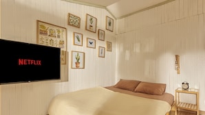 Een slaapkamer met een bed, een aan de muur bevestigde televisie en een klein nachtkastje met een klok.