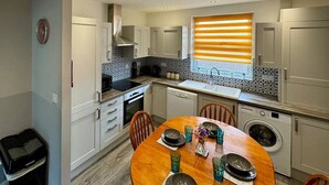 A modern kitchen with white cabinets, a built-in oven, and a dining area with a wooden table and chairs. - Waterloo House – Contractors, Families, Holidays (Nottingham)