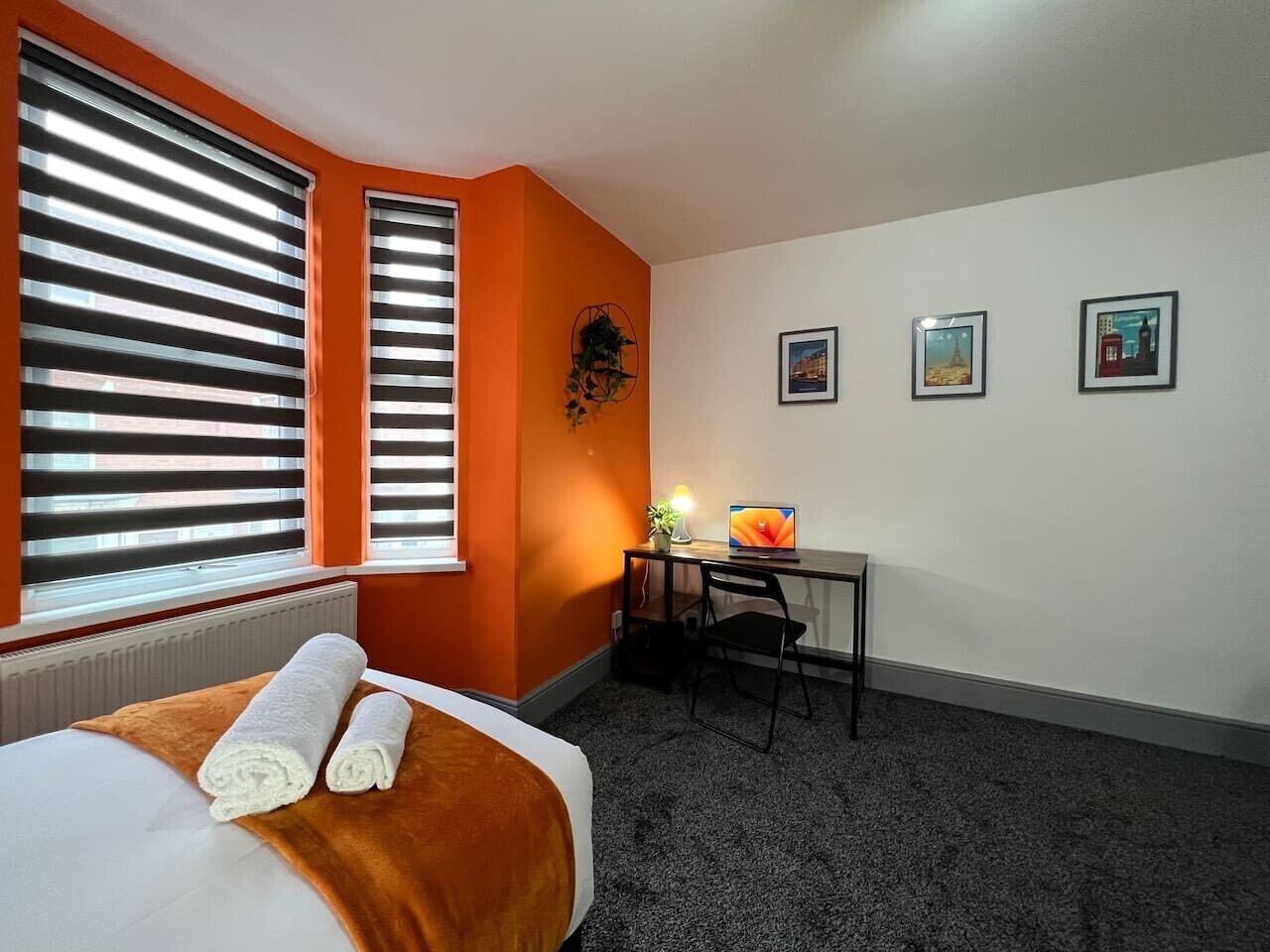 Ein Hotelzimmer mit einem Bett, einem Schreibtisch mit einem Laptop und drei gerahmten Bildern an der Wand.