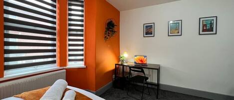 Ein Hotelzimmer mit einem Bett, einem Schreibtisch mit einem Laptop und drei gerahmten Bildern an der Wand.