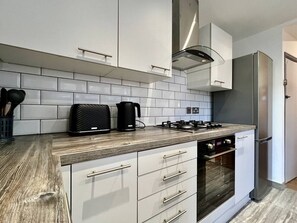 Ett modernt kök med vita skåp, ett kylskåp i rostfritt stål, en inbyggd ugn och en gasspis.