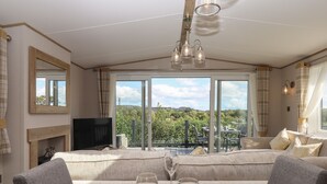 A dining area with a table set for two, a television, and a view of the outdoors. - Hazel Lodge (Newton Abbot)