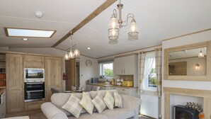 A modern kitchen with built-in appliances, a dining area with a sofa and ottoman, and a fireplace. - Hazel Lodge (Newton Abbot)
