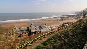Vista sulla costa con spiaggia, una scala di legno che scende e un edificio con una cupola e una torre.