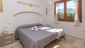 Un dormitorio con cama, mesita de noche, lámpara, ventana con cortinas y vista al exterior.
