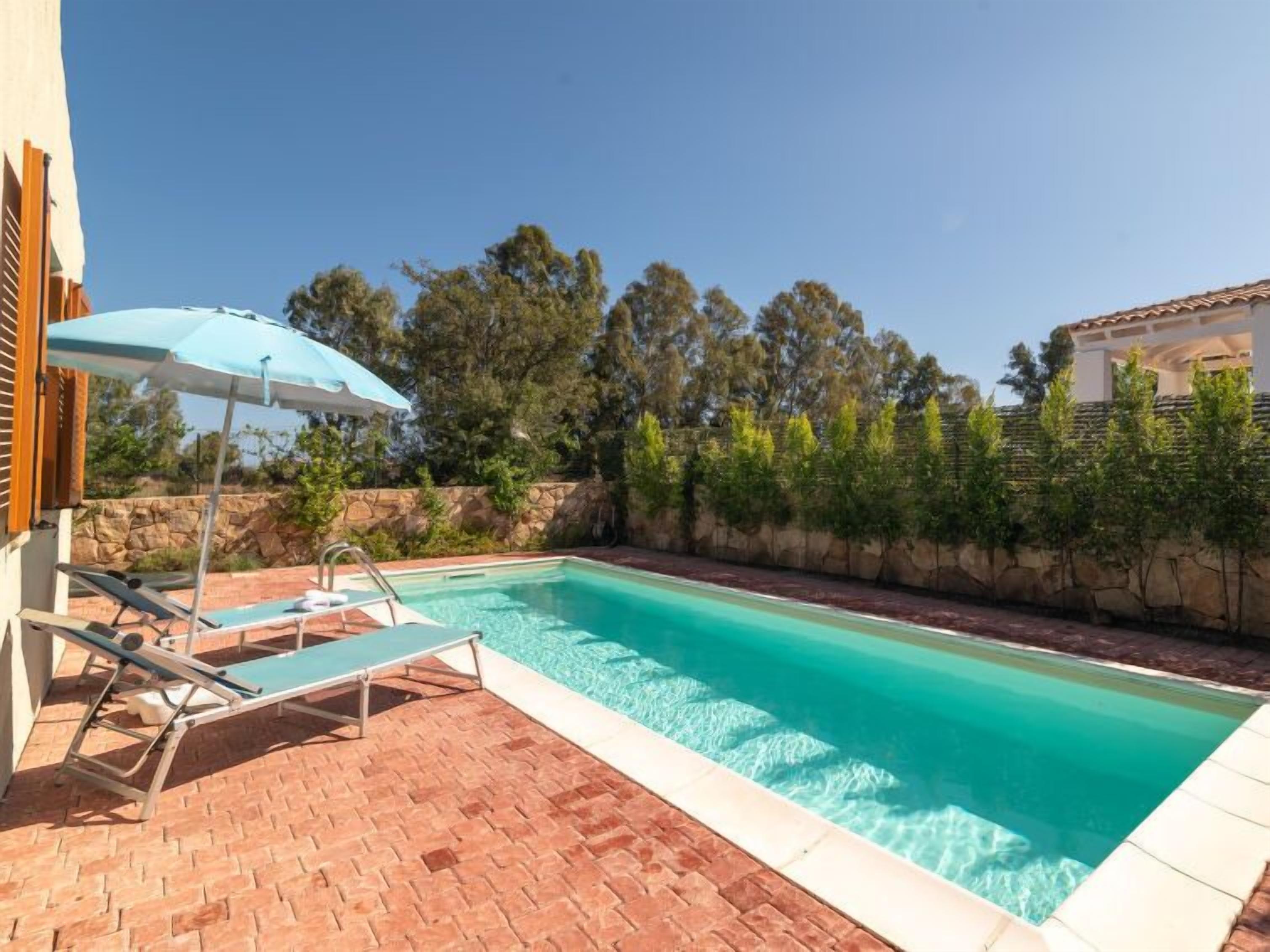 A swimming pool with a tiled deck, a lounge chair, and a sun umbrella.