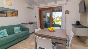 Una sala moderna con un sofá verde, una mesa de comedor con sillas, una zona de cocina con mostrador y un ventanal con vistas al exterior.