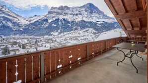 Un balcón de madera con vistas a montañas nevadas y un pequeño pueblo en la falda.