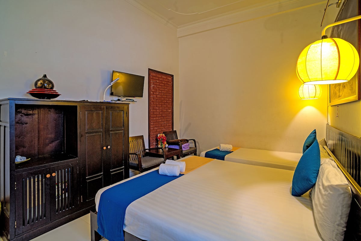 A hotel room with two beds, a TV, a wooden cabinet, and a brick wall.