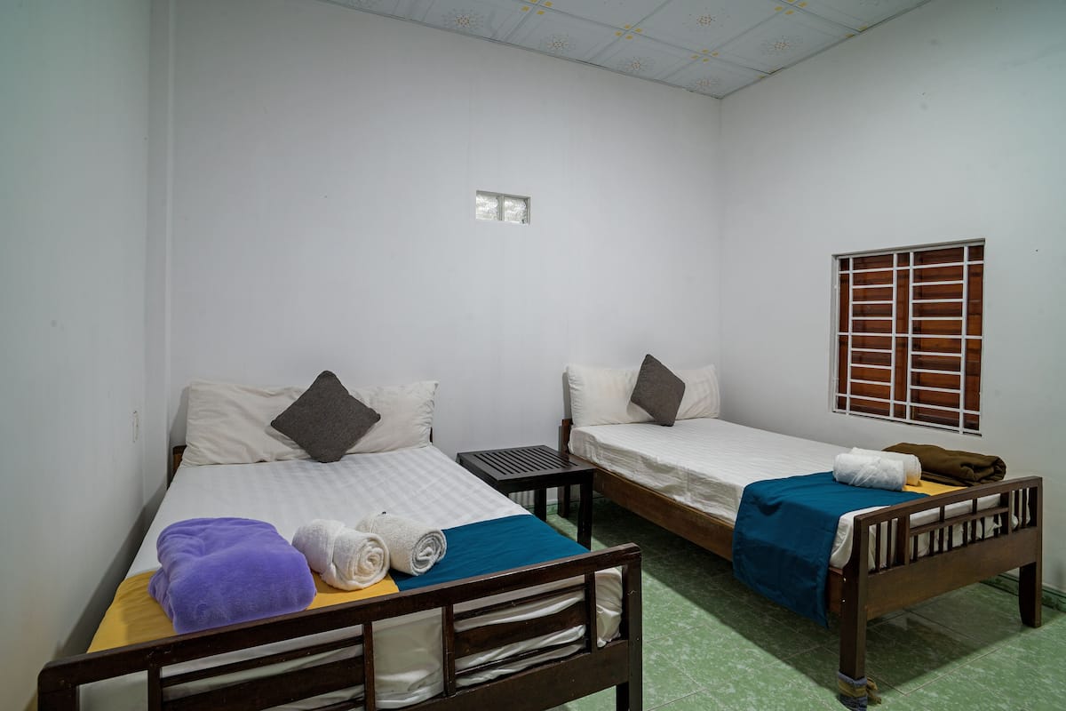 A room with two single beds, each with a pillow and a blanket. There is a small table between the beds.