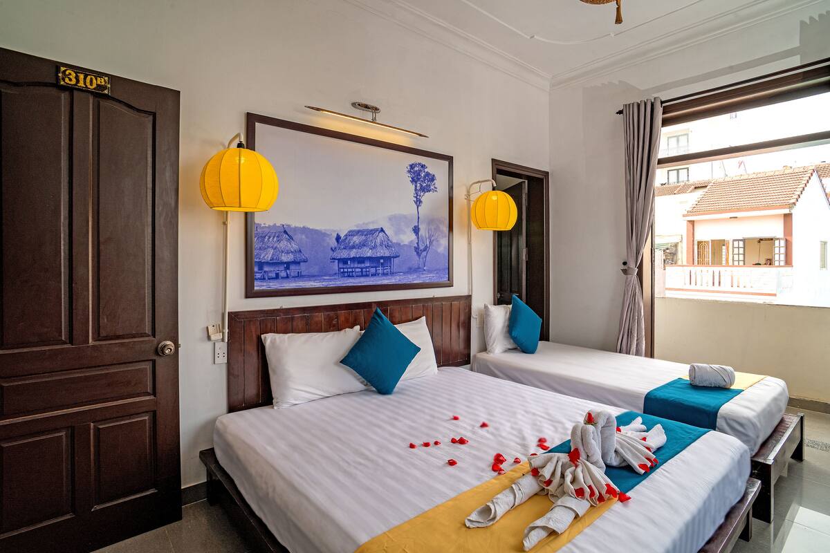 A hotel room with two beds, a large framed picture on the wall, and a balcony with a view of buildings.