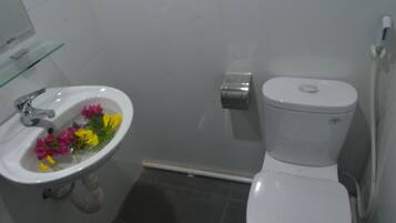 Un baño con lavamanos blanco, inodoro y repisa de vidrio.