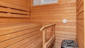 Un sauna avec des murs en bois, un banc, une fenêtre avec des stores et un appareil de chauffage.