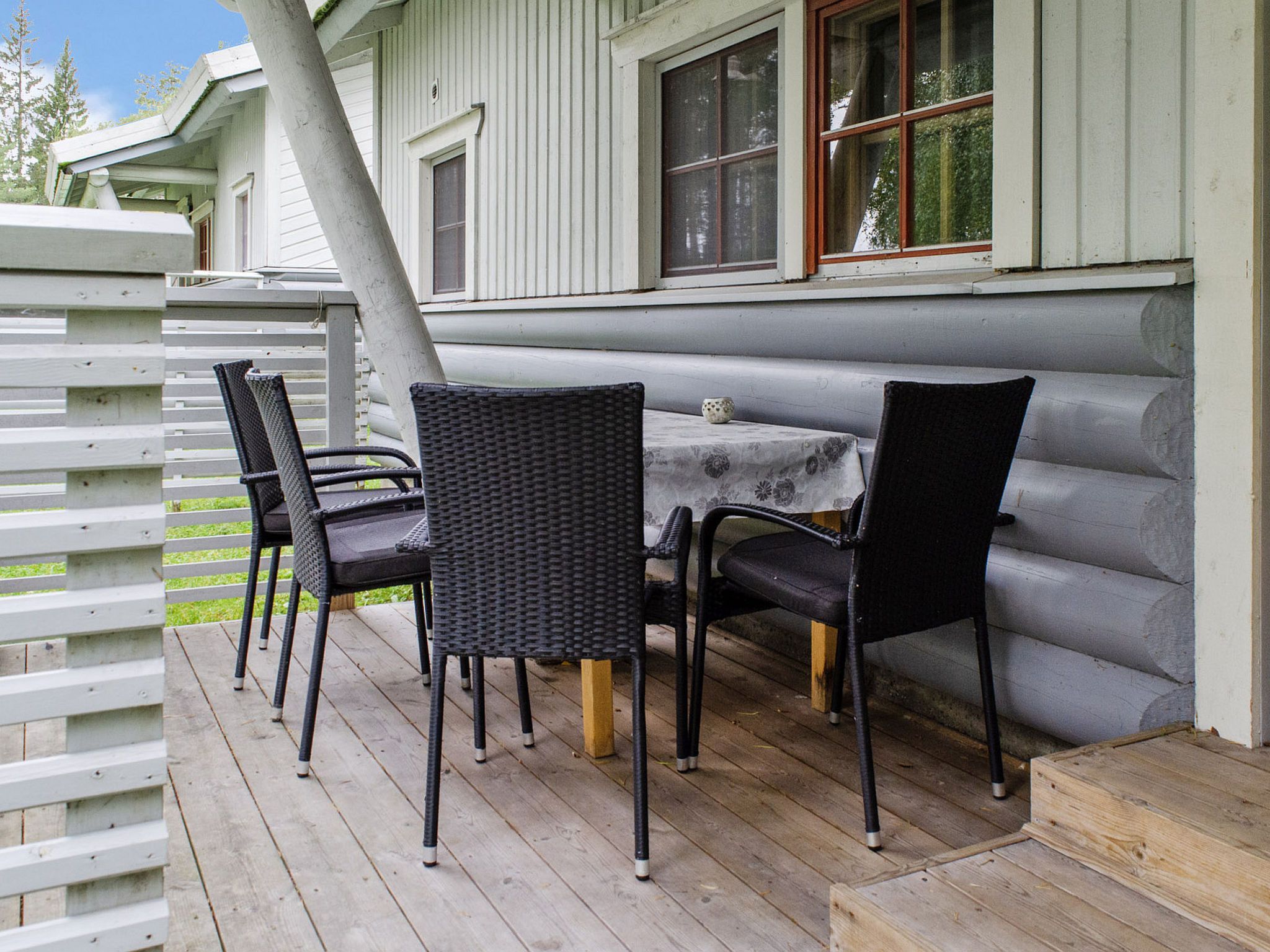A covered outdoor seating area with a table and chairs, a wooden deck, and a white fence.