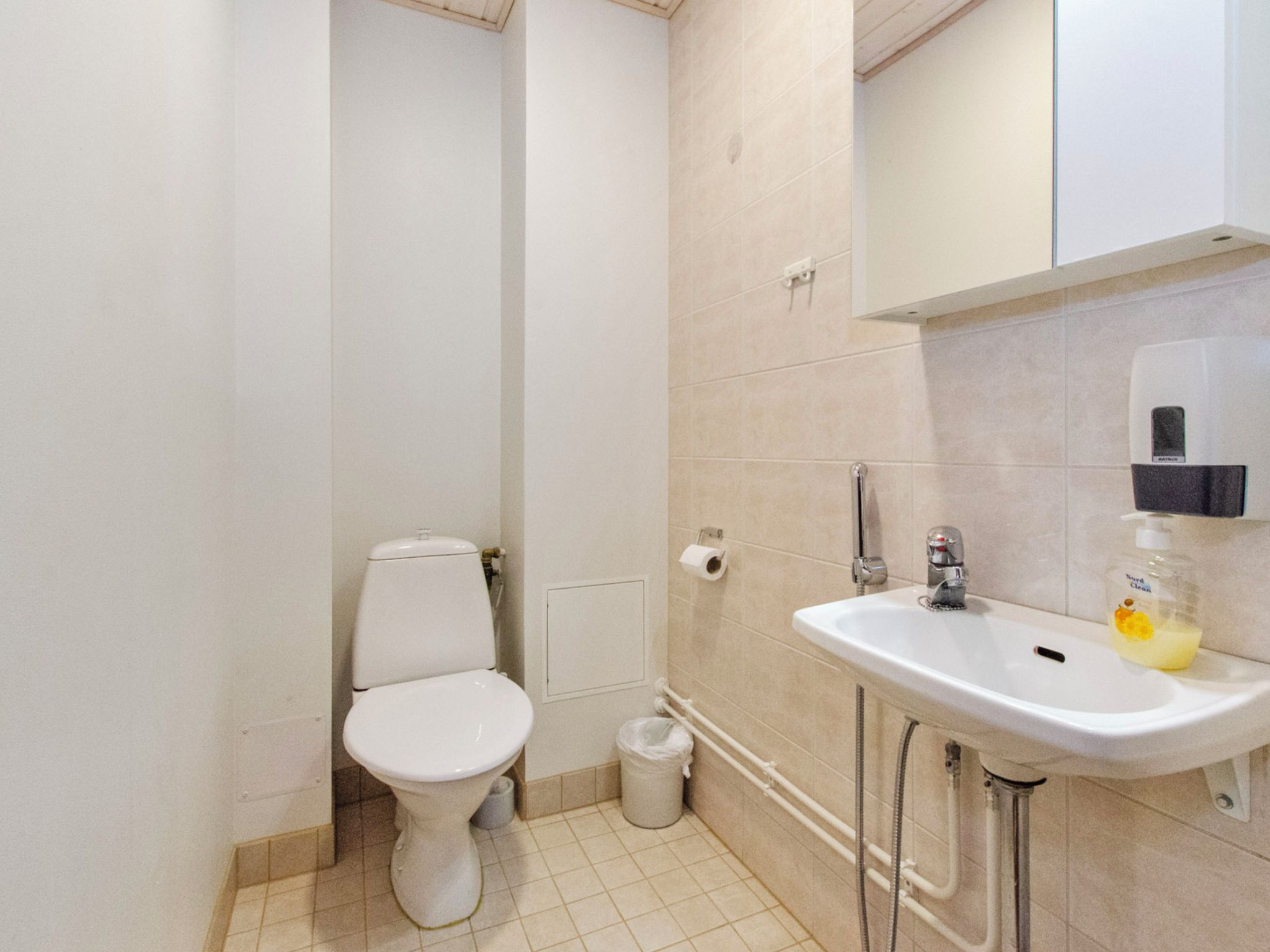 Een kleine, schone badkamer met toilet, wastafel en een zeepdispenser.