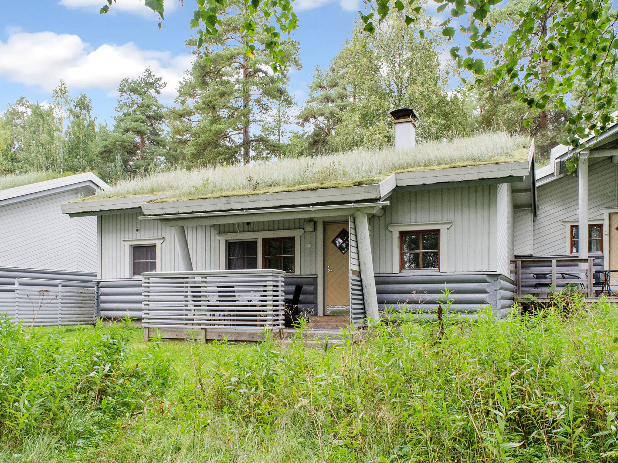 Maalaistyylinen mökki, jossa on ruohokatto, puinen kuisti ja metalliaita.