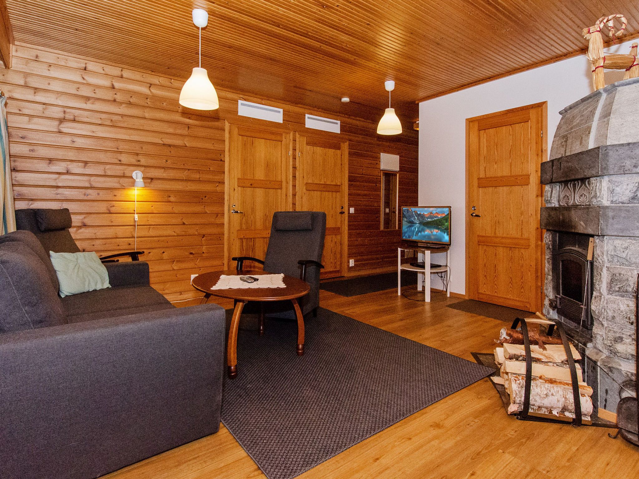 A cozy living room with wooden walls, a fireplace, a sofa, a table, and two chairs.